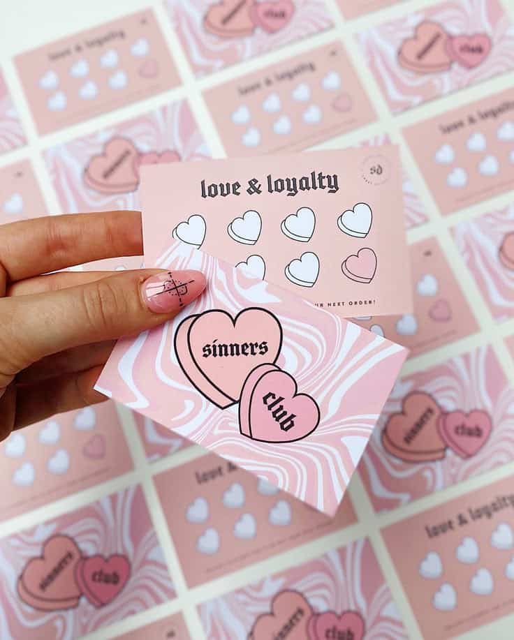 Close-up of pink sinners club and love & loyalty cards with heart designs in a hand over similar cards.