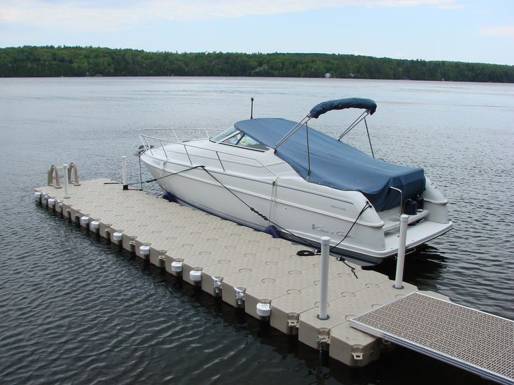 White speedboat docked at a floating pier on a calm lake with a forested shoreline in the background.