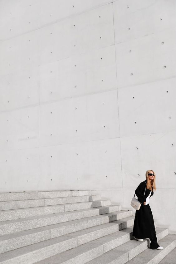 Woman in black dress walking down concrete steps against a minimalist white wall.
