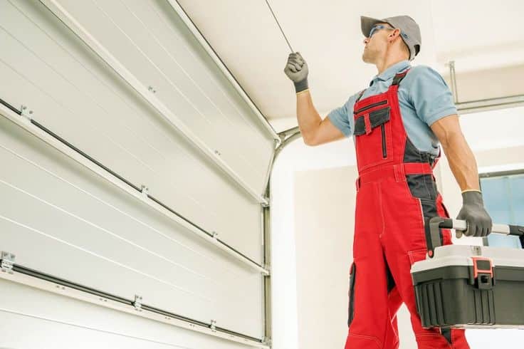 Technician in red overalls adjusting a garage door with a tool kit, ensuring smooth operation and maintenance.