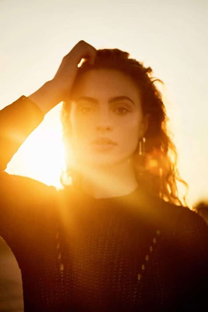 Capture the Magic of Golden Hour_ Essential Tips for Photographers Woman bathed in golden sunlight, standing with her hand on head during sunset. | Sky Rye Design Woman bathed in golden sunlight, standing with her hand on head during sunset.