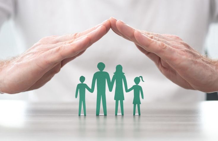 Hands creating a protective roof over paper cutout family, symbolizing security and protection.
