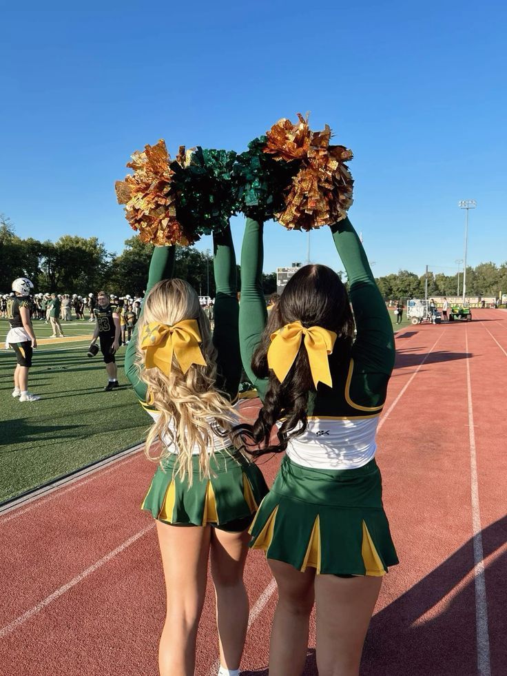 Cheerleaders with pom-poms in green and yellow uniforms on a sunny sports track, ready for a pep rally.