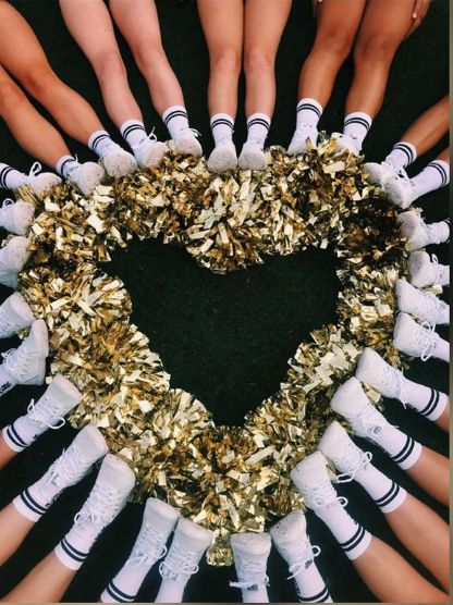 Cheerleaders' legs and shoes form a circle with gold pom-poms creating a heart shape in the center.