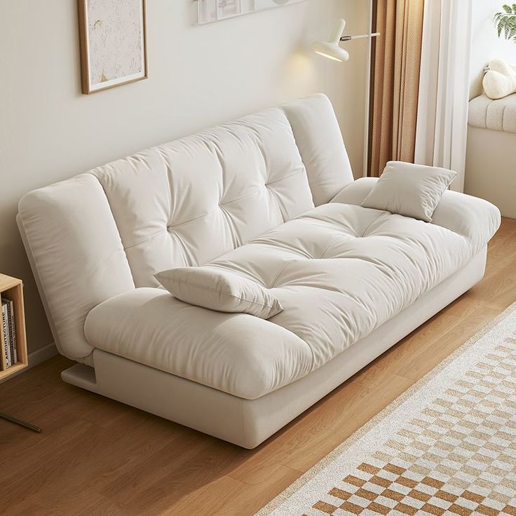 Cream-colored tufted sofa bed in stylish living room with wooden floor and modern decor. Plush cushions add comfort.