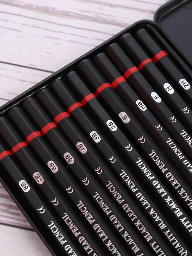 Set of black lead pencils in various grades arranged neatly in a box on wooden background.
