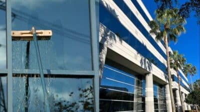 Modern glass office building with palm trees reflected, showcasing architectural design and sunny weather.