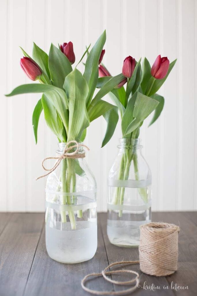 Red tulips in glass jars with twine, rustic home decor on wooden table.
