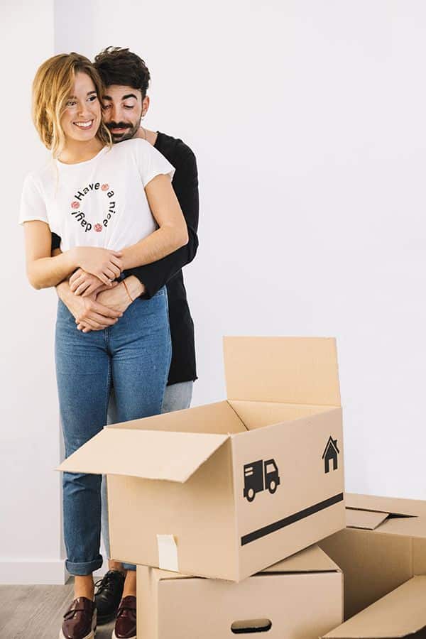 Couple hugging while moving into a new home with cardboard boxes around.