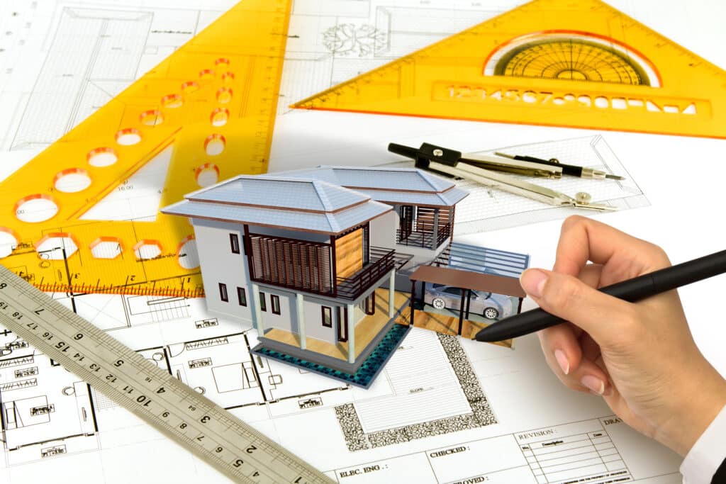 Architectural design process with house model on blueprints, ruler, and drawing tools.