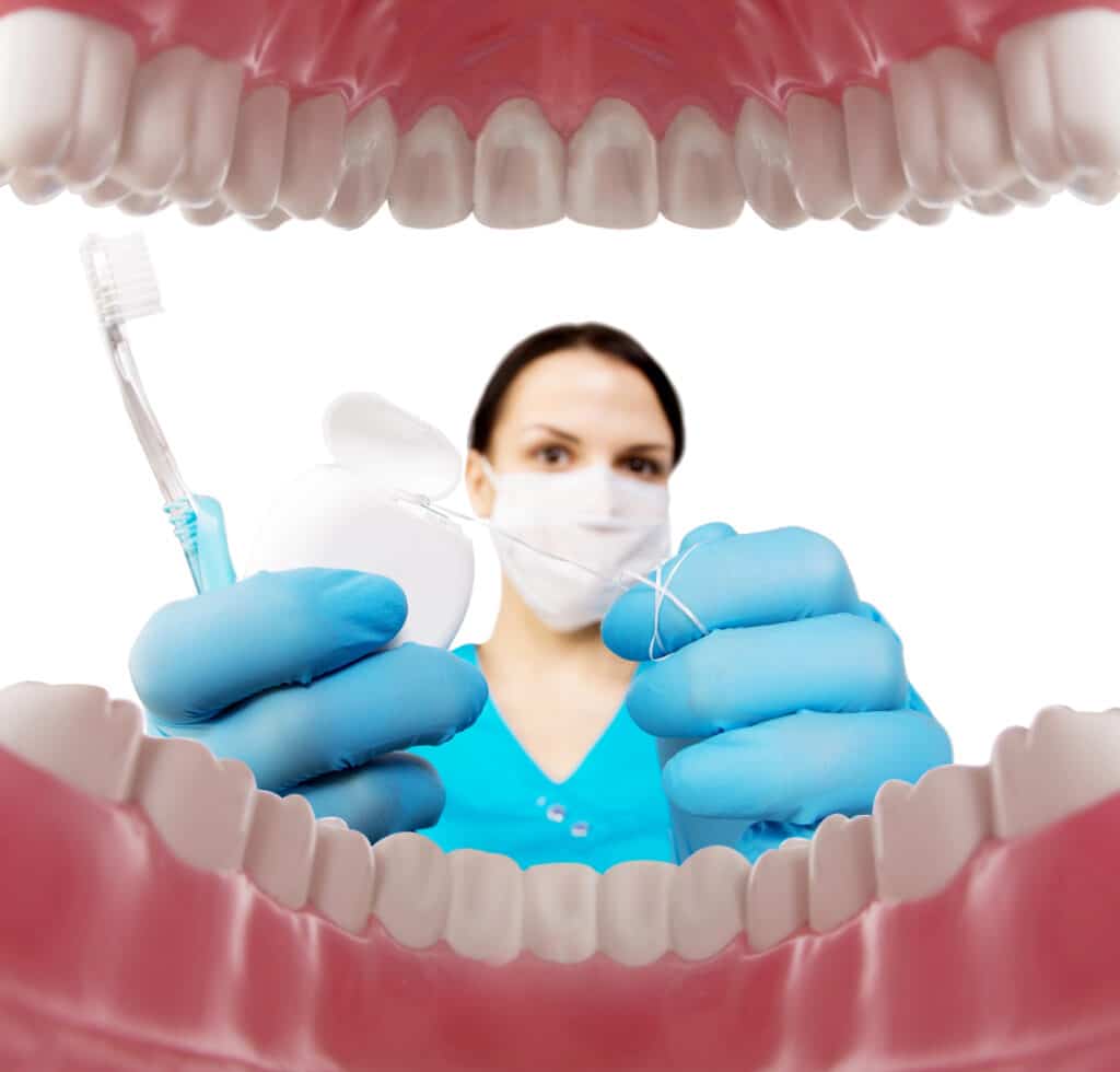 Dentist with mask holding toothbrush and floss between teeth, emphasizing oral hygiene and dental care.