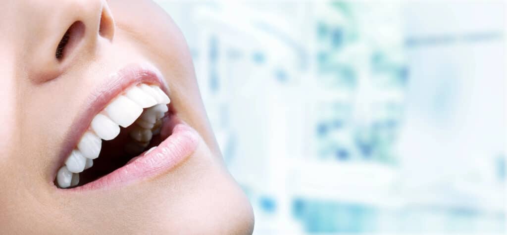Close-up of a smiling person showing white teeth with a dental clinic background.