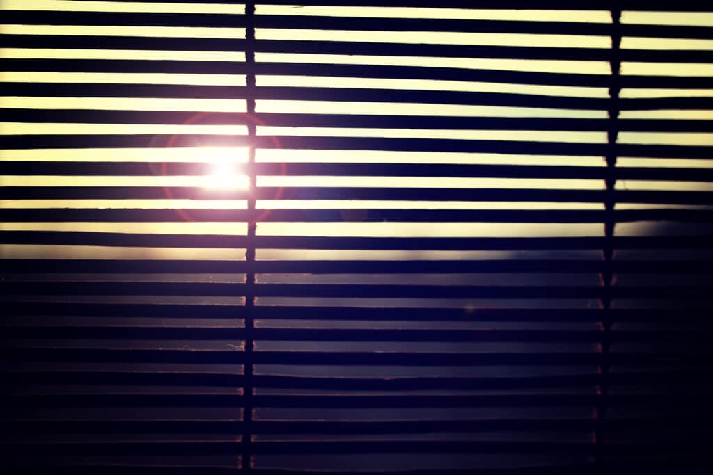 Sunlight peeking through window blinds, creating a warm and serene indoor atmosphere.