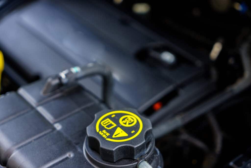 Close-up of car engine oil cap with warning symbols and yellow text on black surface.