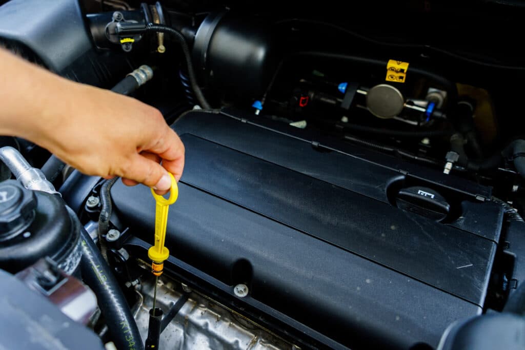 Depositphotos_188072300_XL Hand checking oil level with dipstick in car engine compartment for maintenance. | Sky Rye Design Hand checking oil level with dipstick in car engine compartment for maintenance.