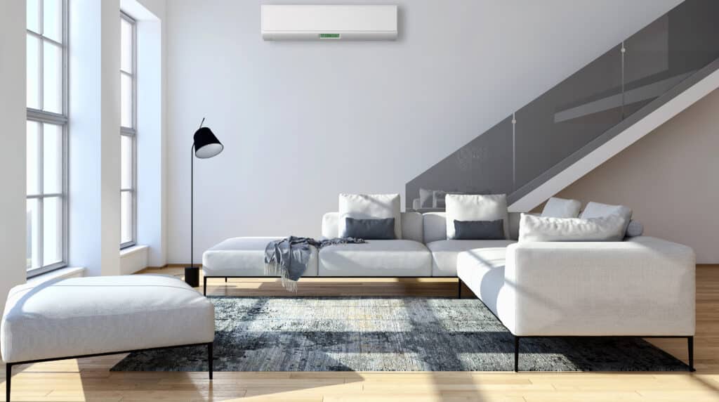 Depositphotos_201951084_XL Modern living room with white sectional sofa, large windows, and wall-mounted air conditioner under sleek staircase. | Sky Rye Design Modern living room with white sectional sofa, large windows, and wall-mounted air conditioner under sleek staircase.