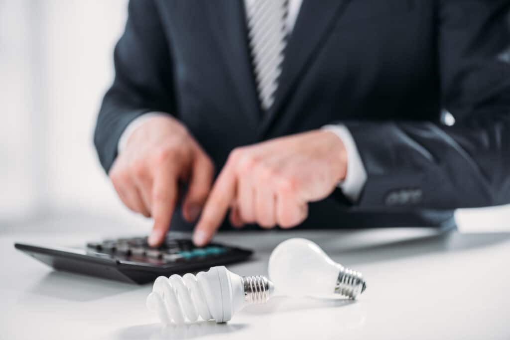 Businessman calculating energy savings with light bulbs on desk.