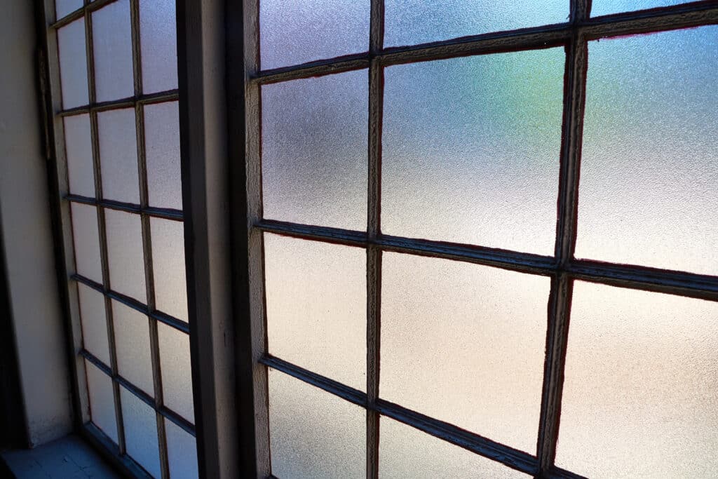 Frosted glass window panels with metal grid design, diffusing colorful light through textured surface.