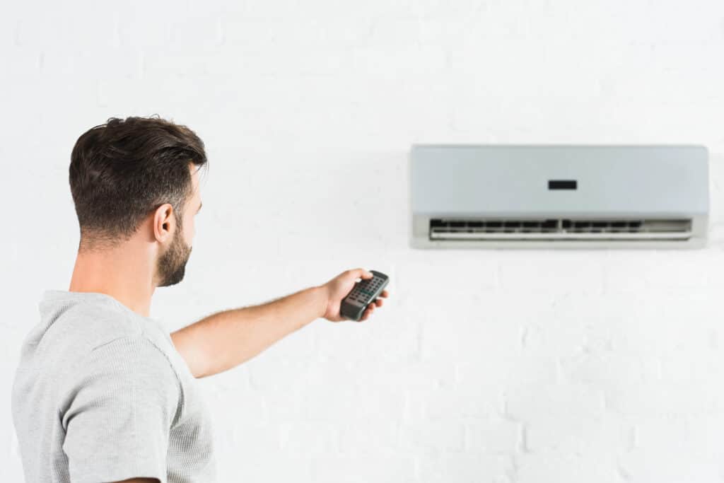 Man using remote control to operate wall-mounted air conditioner.