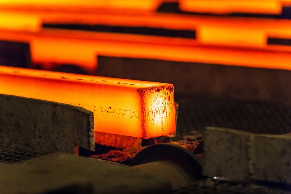 Glowing hot steel bars cooling on a conveyor belt in a steel mill, showcasing the metal production process.