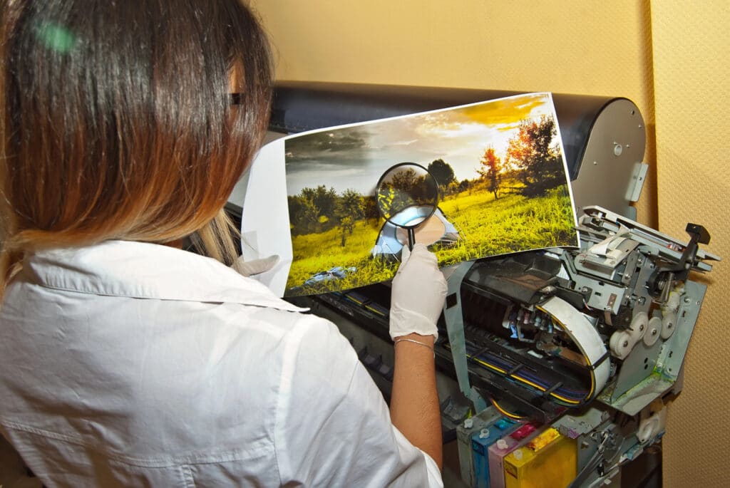 Depositphotos_322153100_XL Person examining a printed landscape photo with a magnifying glass next to a professional printer. | Sky Rye Design Person examining a printed landscape photo with a magnifying glass next to a professional printer.