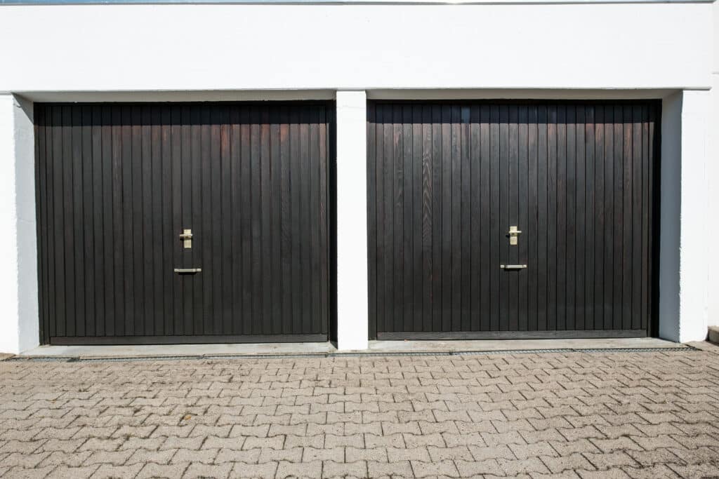 Double black garage doors on white building facade with paved driveway.