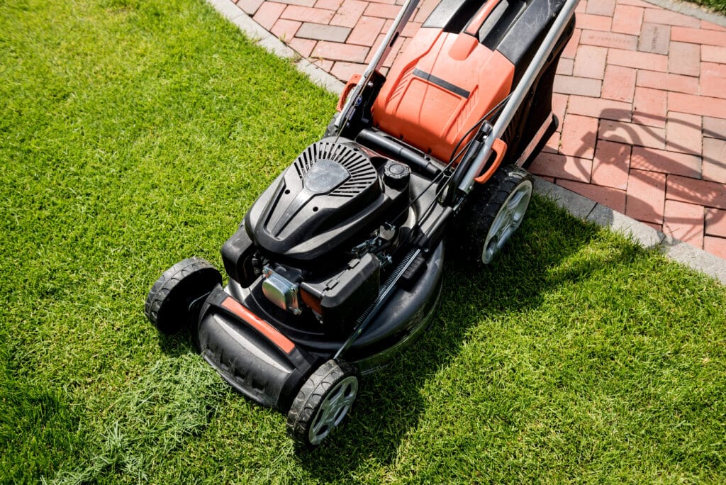 Red and black lawn mower on green grass near a brick path, perfect for garden maintenance and landscaping tasks.