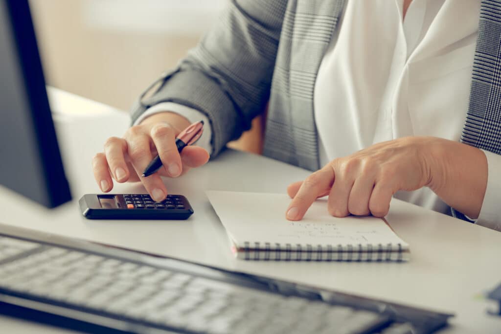 Person in business attire using calculator and notepad at desk for financial work.