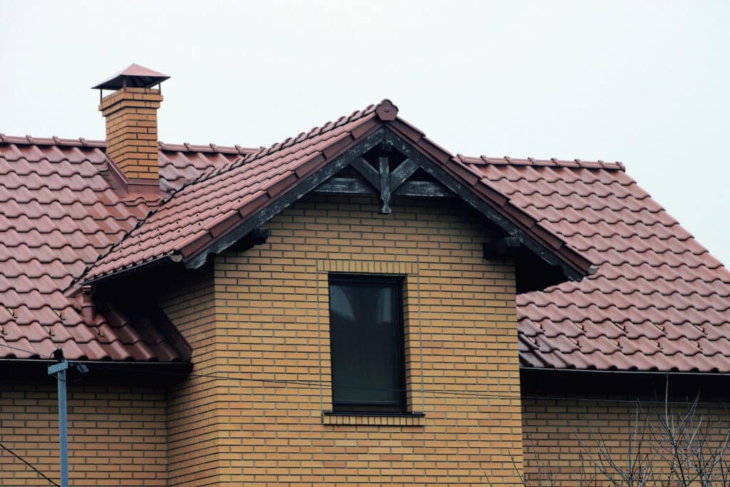 Brick house with red tile roof and chimney against a clear sky.