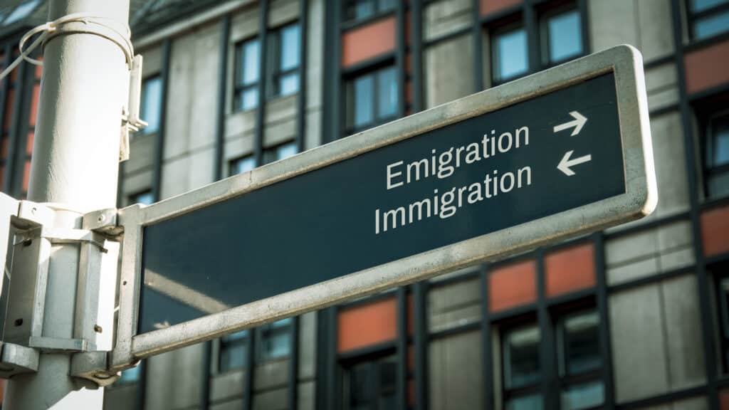 Signpost showing directions for emigration and immigration against a building background.