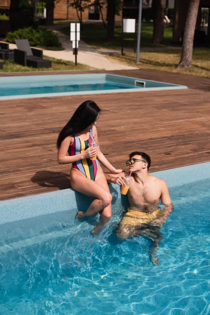 Couple relaxing by poolside with drinks on a sunny day, enjoying summer vacation.
