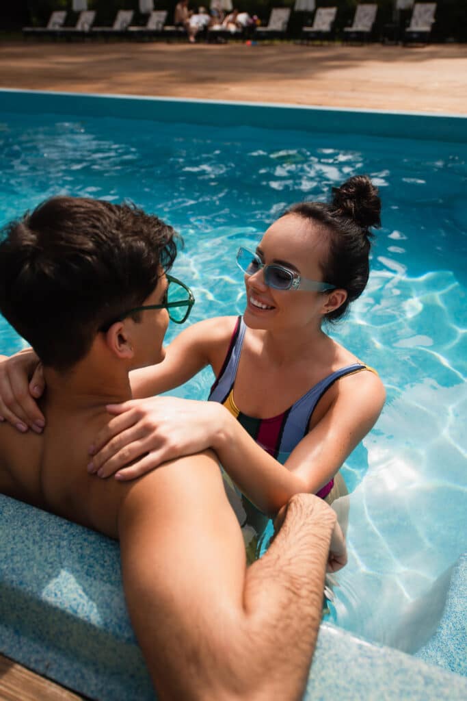 Couple enjoying a sunny day at the pool, smiling and wearing sunglasses.