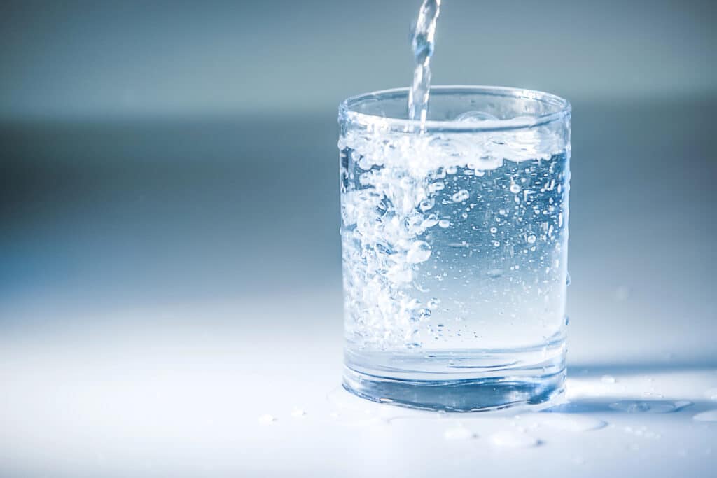 Glass of water being poured with bubbles on a blue background.