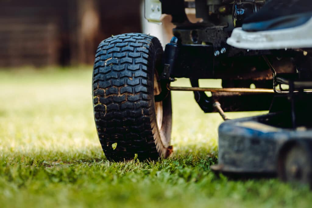 Close-up of a riding lawn mower wheel on green grass, highlighting outdoor lawn care equipment.
