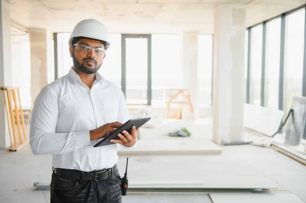 Asian Engineer standing on site construction posting confident Engineer construction happy job success Construction site manager in hard hat uses tablet for project planning. | Sky Rye Design Construction site manager in hard hat uses tablet for project planning.