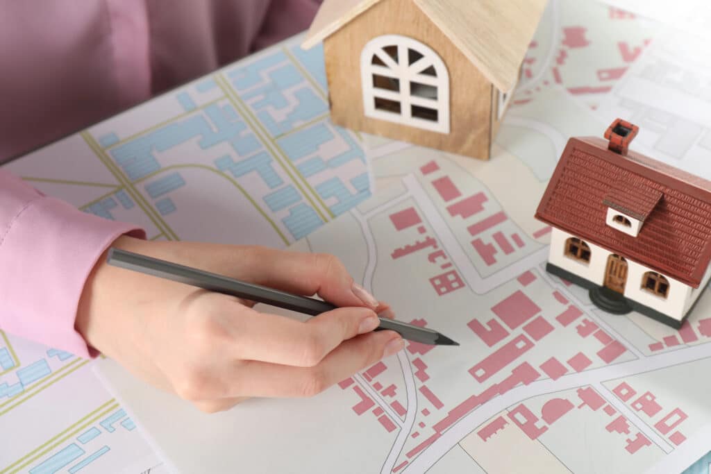 Hand drawing on a city map with small house models, illustrating real estate planning and development.