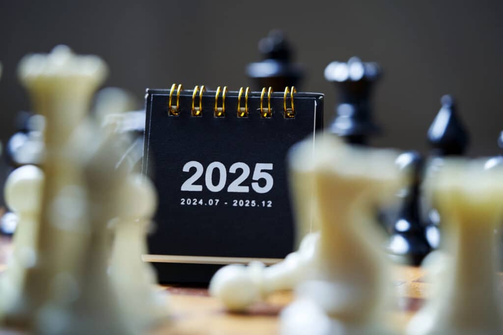 Desk calendar displaying 2025 surrounded by chess pieces, symbolizing strategic planning and future goals.
