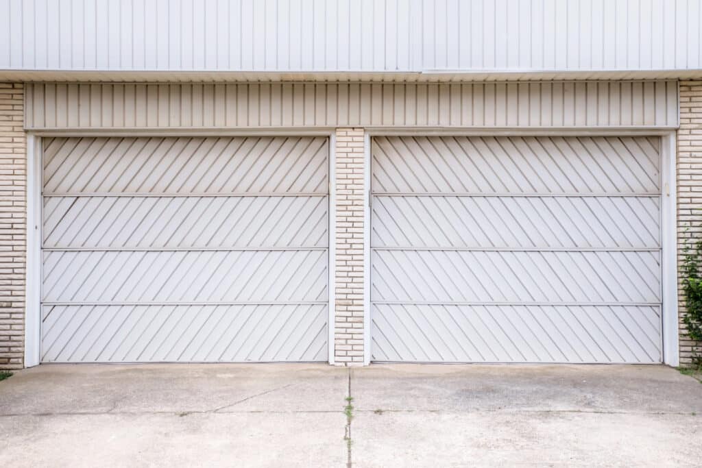 Double garage doors with white diagonal paneling, framed by brick columns.