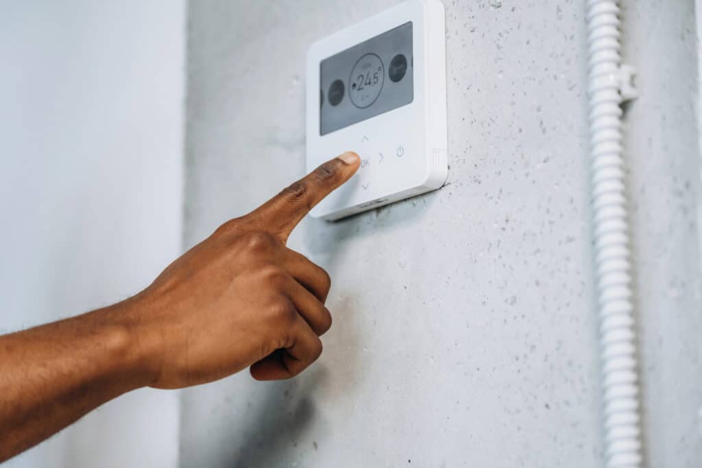 Finger adjusting digital thermostat on wall for home temperature control.