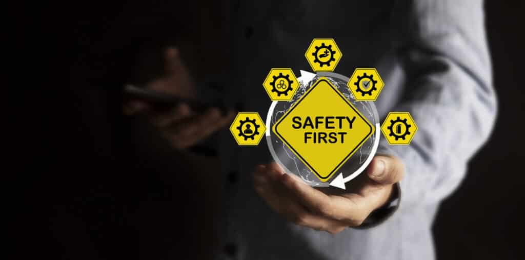 Hand holding 'Safety First' sign with safety icons, emphasizing workplace precautions and security measures.