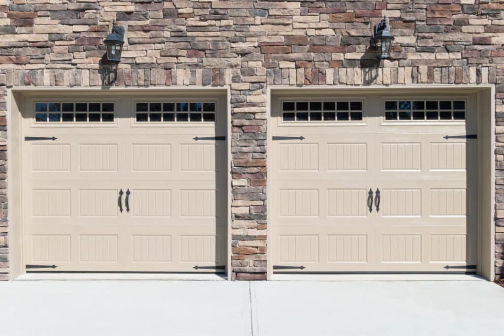 Stone facade with two beige garage doors and decorative lantern lights.