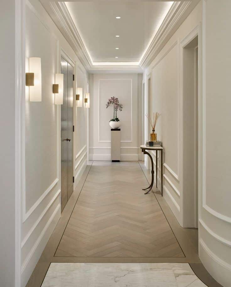 Elegant hallway with herringbone wood floor, wall sconces, and decorative accents.