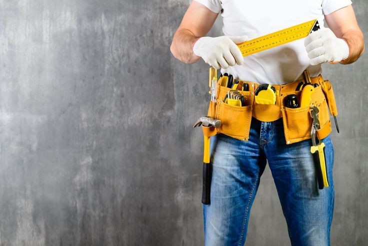 Handyman with tool belt and measuring tape, ready for construction work against gray background.