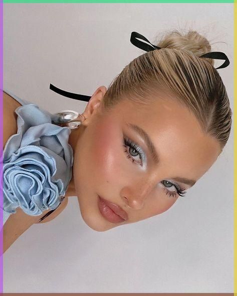 Close-up of a woman with elegant makeup and a blue floral accessory, featuring a sleek bun tied with a black ribbon.