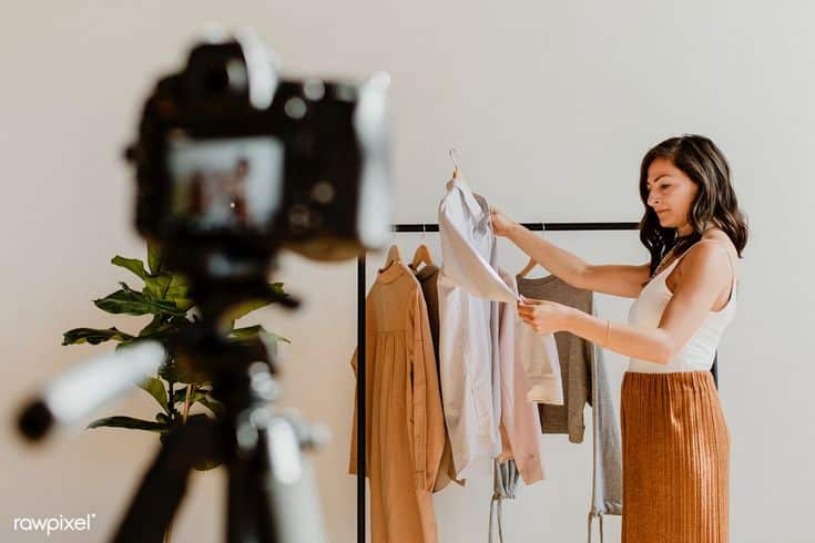 Woman styling clothes in front of camera for fashion blog recording.