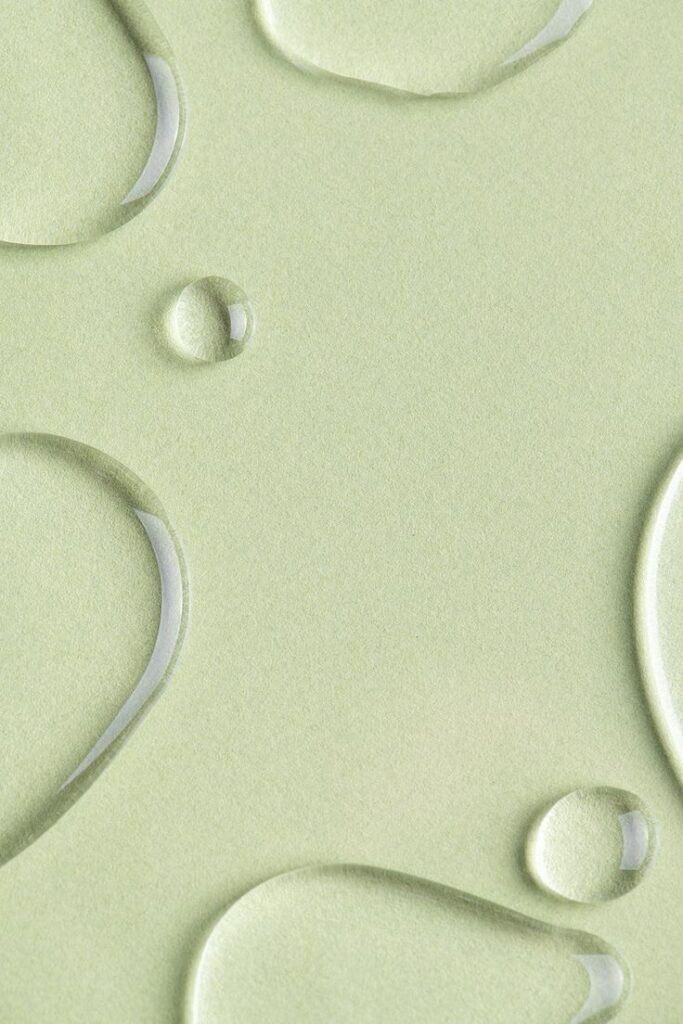 Water droplets on a light green surface, showcasing texture and reflection.
