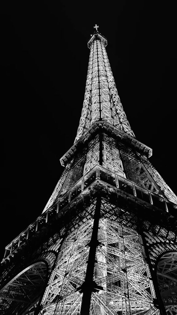 Black and white view of the Eiffel Tower illuminated at night, upward perspective against a dark sky.