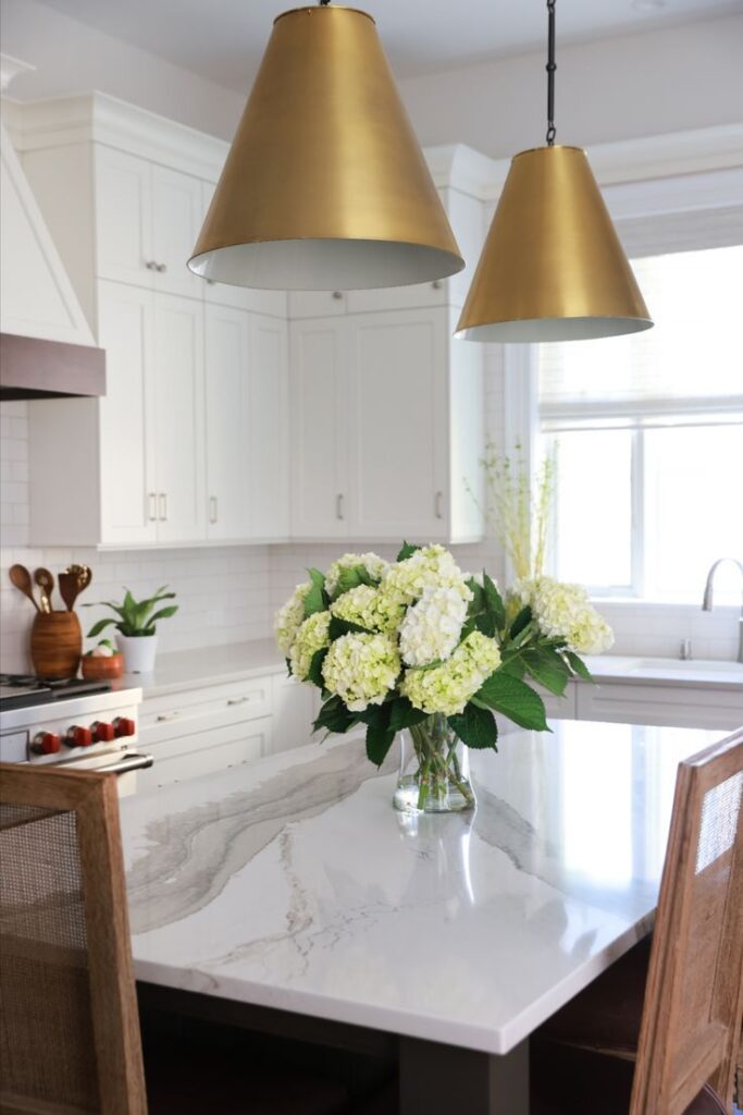 Modern kitchen with marble island, gold pendant lights, and vase of white hydrangeas.