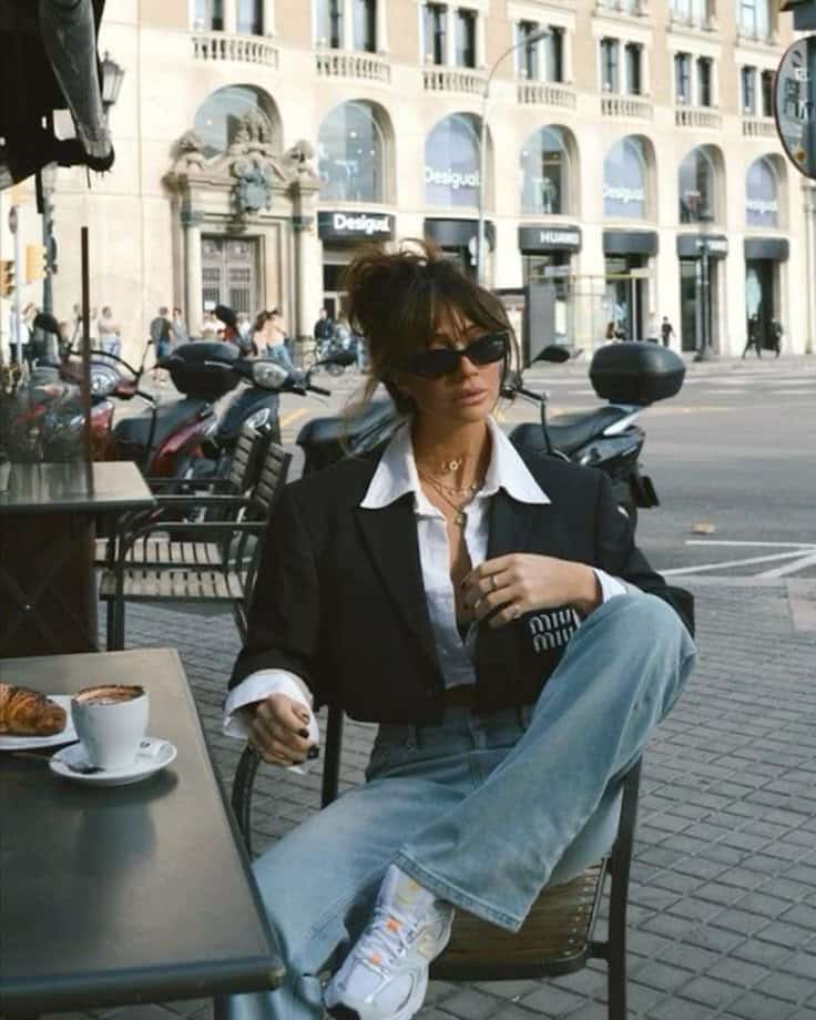 Chic woman in sunglasses enjoys coffee at a stylish outdoor cafe in an urban setting.