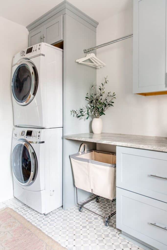 Modern laundry room with stacked washer dryer, storage cabinets, hanging rod, and rolling laundry basket.